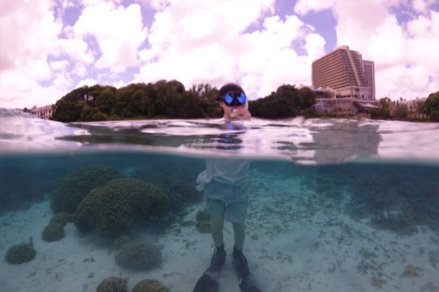 Half-underwater shot of Andrew in snorkel gear standing over the reef in Tumon Bay