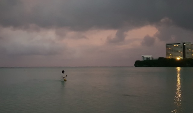 Andrew standing waist-deep in Tumon Bay at sunrise, looking out under pink clouds
